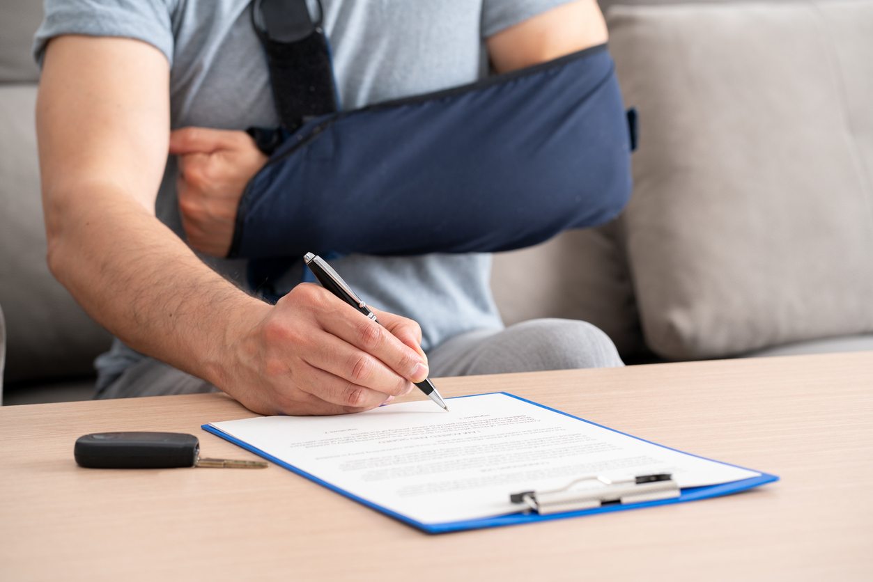 Man with broken arm in sling signing an insurance document after car accident